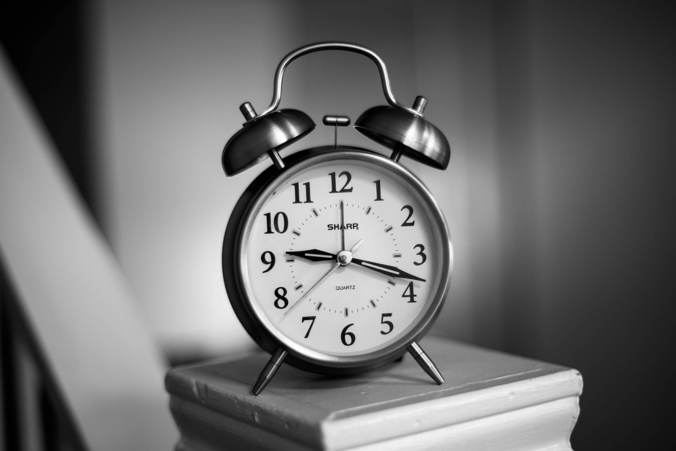 Close-up of a monochrome analogue alarm clock, showcasing time precision.