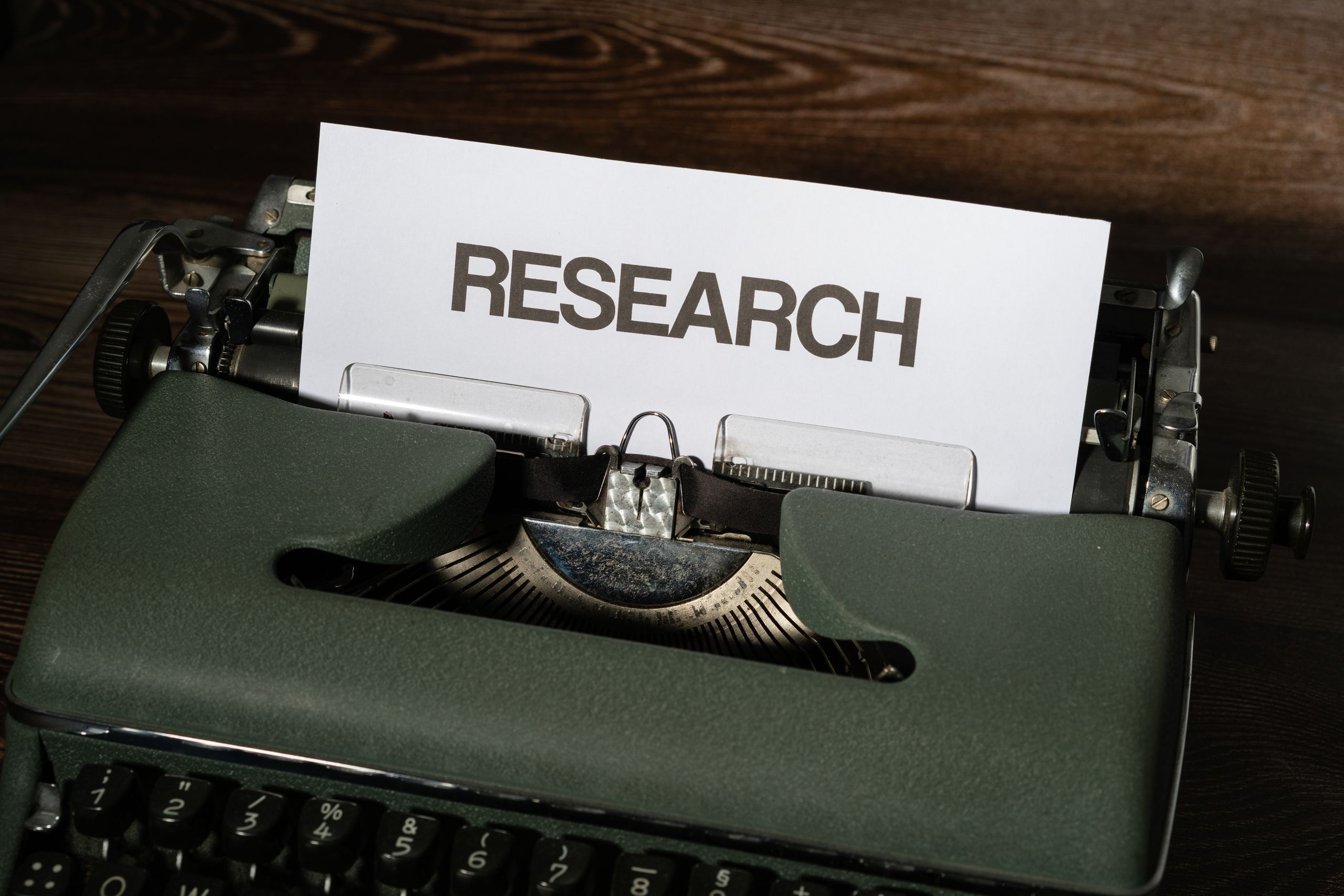 Close-up of a vintage typewriter with a paper labeled 'Research' inserted, on a wooden surface.