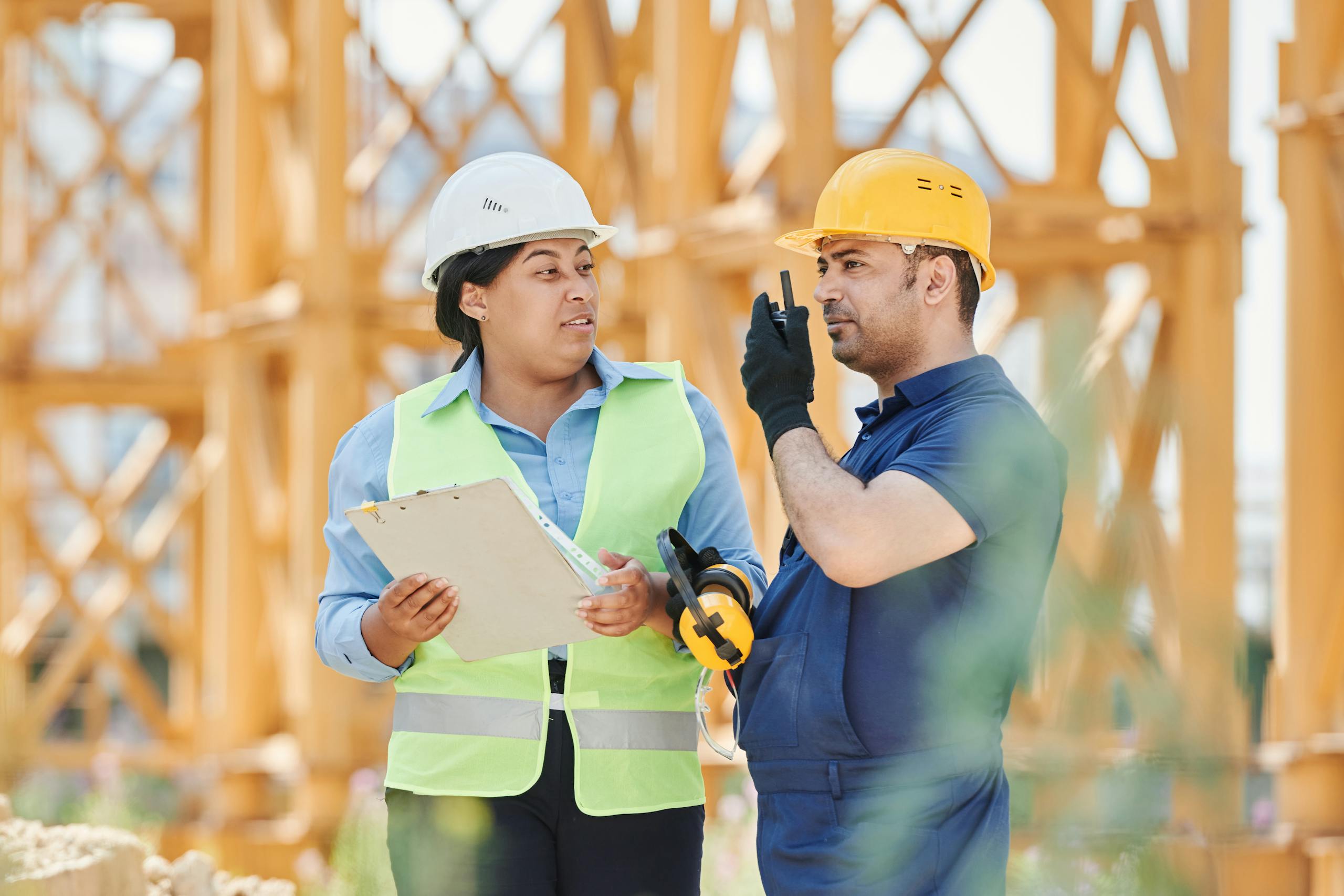 Engineers in safety gear discussing a construction project outdoors with visible scaffolding.