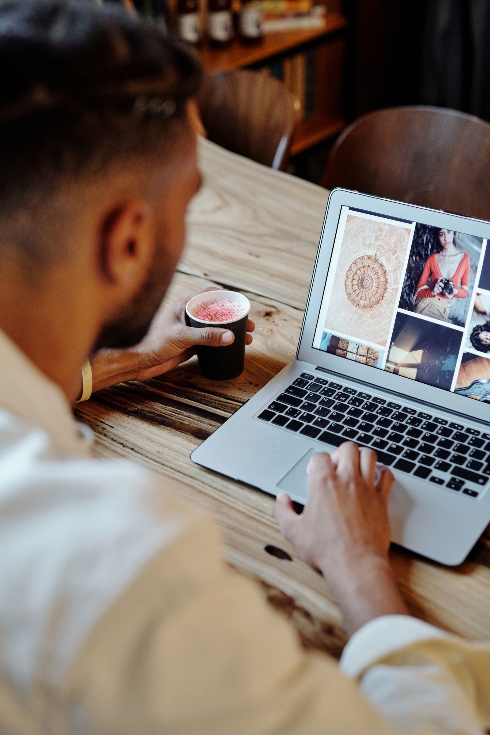 Man focused on work on laptop with artistic images and coffee in a cozy setting.